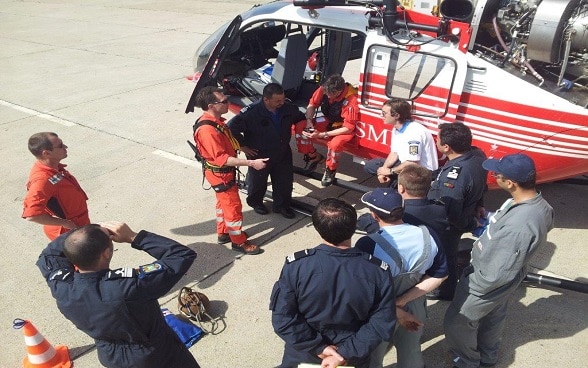 Des hommes se tiennent près d’un hélicoptère sur un aérodrome. 