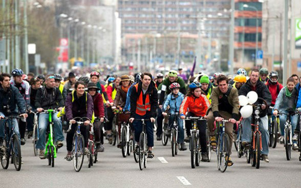 Eine grosse Gruppe von Fahrradfahrern und Fahrradfahrerinnen fährt auf der ganzen Strasse in einer Stadt.