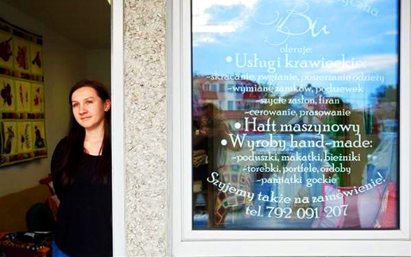 A young entrepreneur stands in the doorway of her sewing and textile goods business.