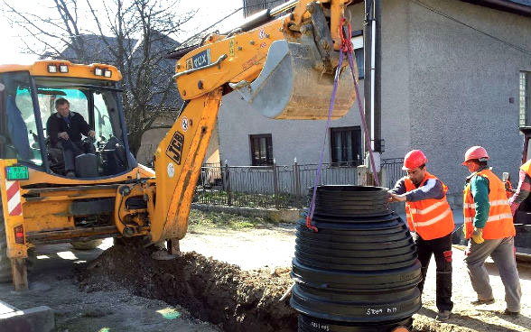 Ein Mann im Bagger und drei weitere Bauleute arbeiten an einem Kanalisationsnetz.